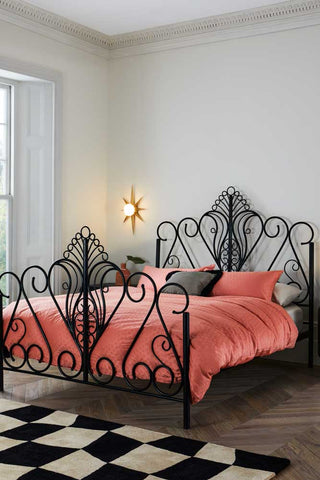 The Peacock Bed styled with pink bedding, a checkerboard rug and a wall light.