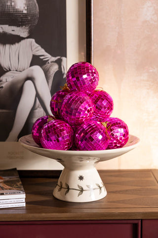 Several Pink Disco Ball Christmas Tree Decorations styled on a cake stand on a wooden sideboard.