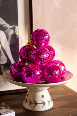 Several Pink Disco Ball Christmas Tree Decorations styled together on a cake stand.