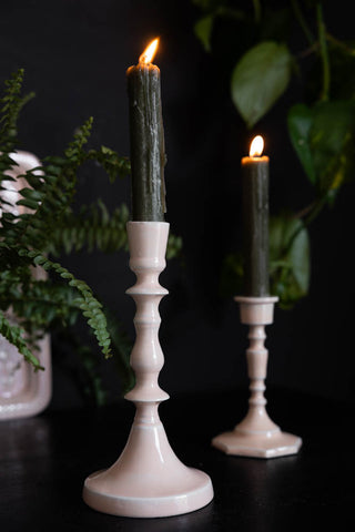 The Short and Tall Pink Enamel Cast Style Candlestick Holders displayed together with lit candles inside, styled with plants in the background.