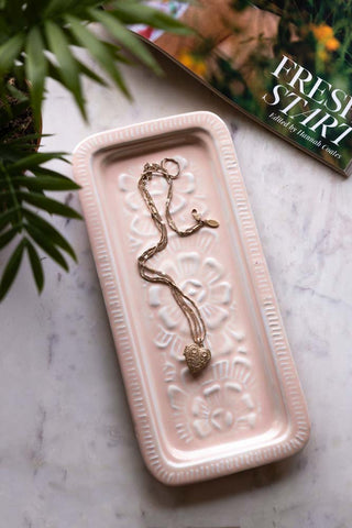 The Pink Enamel Cast Style Trinket Tray displayed on a white marble table with a necklace inside, styled with a magazine and a plant.