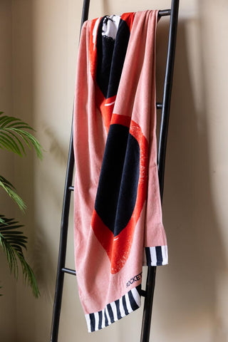 The Pink Glasses Beach Towel displayed hanging on a black rail next to a plant.