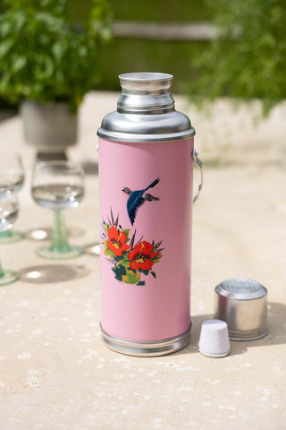 Lifestyle image of the Pink Painted Bird Decorative Flask with the lid off on an outdoor table.