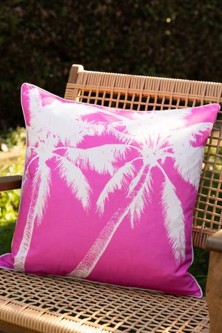 The Pink Palm Tree Outdoor Cushion styled on a wicker chair outdoors.