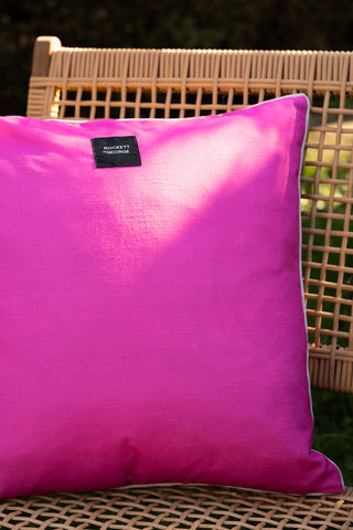 The reverse side of the Pink Palm Tree Outdoor Cushion, displayed outdoors on woven chair.