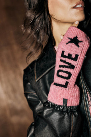 The love handwarmer from the The Pink Peace & Love Handwarmers set, showing the word "love" and a star in black against a pink woven fabric. The handwarmer is worn by a woman wearing a black leather jacket. 