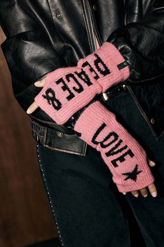 The Pink Peace & Love Handwarmers set shown worn with studded jeans and a black leather jacket. The handwarmers are pink with black text and icons. 