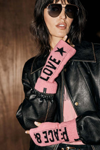 The Pink Peace & Love Handwarmers, with one showing "peace &" in black against the pink fabric and the other showing "love" with a star in black against the pink fabric. The handwarmers are shown on a woman eating a leather jacket and aviator glasses. 