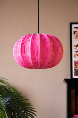The Hot Pink Pleated Fabric Ceiling Light hanging with a plant, fireplace and art print in the background.