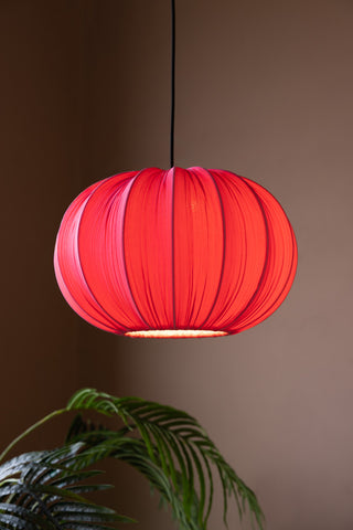 The Hot Pink Pleated Fabric Ceiling Light switched on and hanging above a plant.