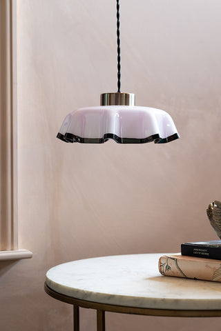 The Pink Pleated Glass Easyfit Ceiling Light Shade shown against plastic pink walls, hanging over a coffee table. 