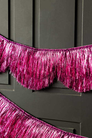 The Pink Scalloped Tinsel Garland styled on a black panelled wall.