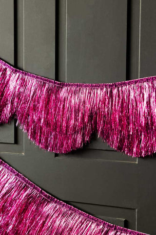 The Pink Scalloped Tinsel Garland styled on a black panelled wall.