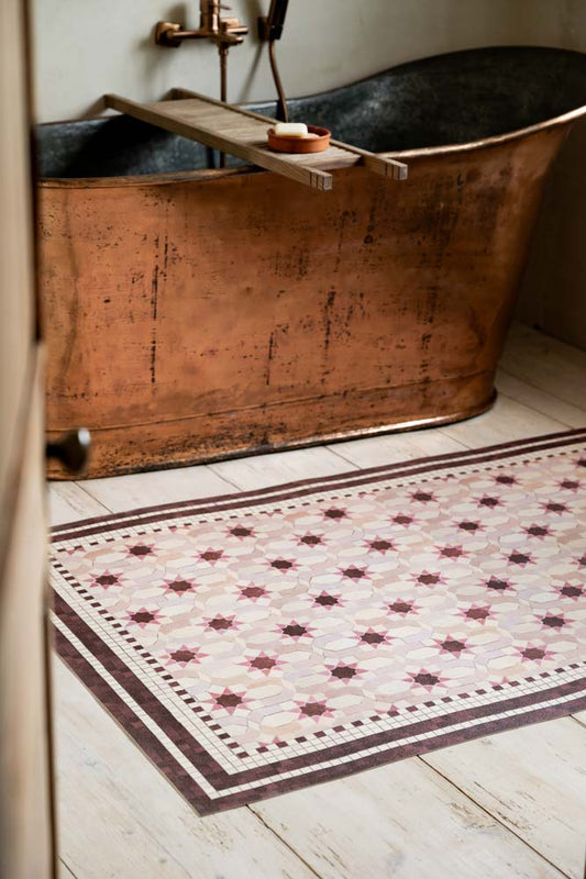 The Pink Star Durable Floor Mat is shown in a bathroom, next to a copper bath on white wood floors. 