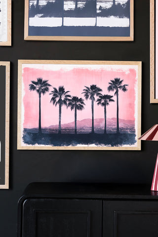 Framed artwork of palm trees with a pink and blue gradient on a dark wall.