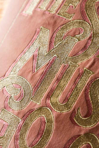 Pink fabric with gold embroidered text on a pink background