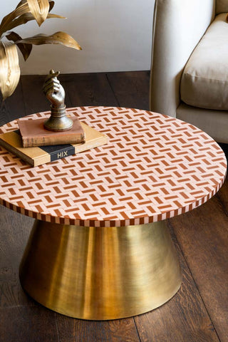 The Pink & Caramel Inlay Coffee Table styled with some books and an ornament on, in front of a chair and plant.