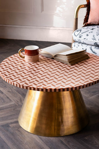 The Pink & Caramel Inlay Coffee Table with a mug and open book on with a chair in the background.