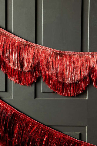 The Pink & Red Scalloped Tinsel Garland styled on a black panelled wall.