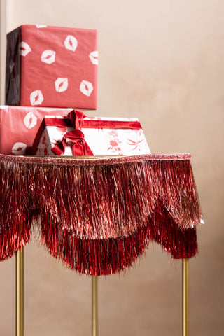 The Pink & Red Scalloped Tinsel Garland styled around the edge of a table with presents on.