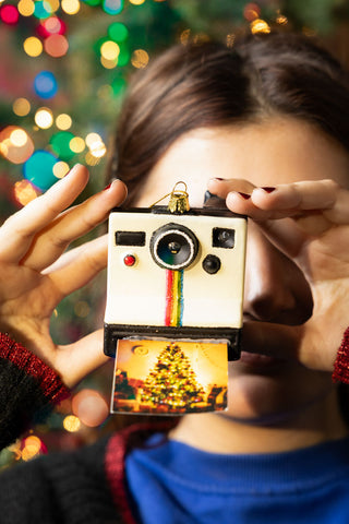 A model holding the Polaroid-Inspired Camera Christmas Tree Decoration in front of their face, pretending to take a photograph.