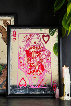 The Queen Of Hearts Decorative Playing Card decorative Mirror styled on a black sideboard with another mirror, a crystal, a lit candle in a gold candlestick holder and some greenery.