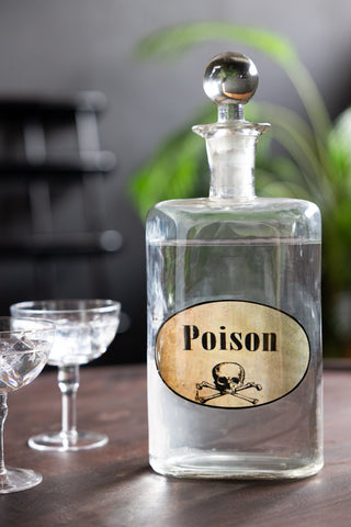 The Quirky 'Poison' Glass Decanter styled on a wooden surface with some champagne glasses.