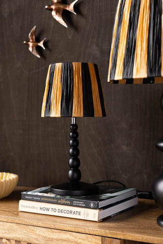 The Small Black Bobbin Bedside Table Lamp on a wooden sideboard.