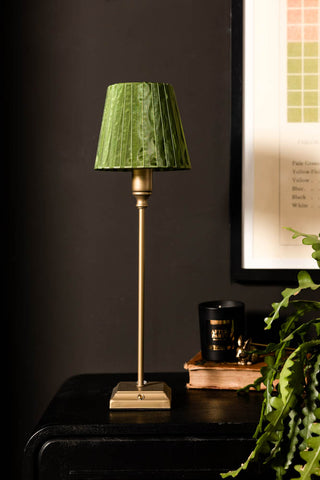 Table lamp with a green pleated shade on a dark surface, with a framed picture in the background.