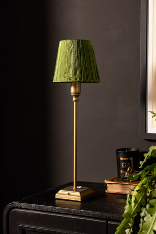 Table lamp with a green shade on a dark surface against a dark wall.