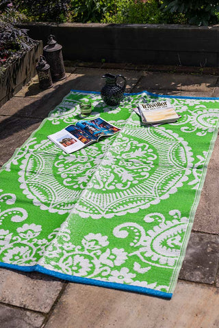 The Recycled Vintage Design Outdoor Rug in Green outdoors, with magazines, a jug and glass.