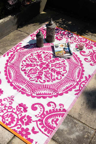 The Recycled Vintage Design Outdoor Rug in Pink displayed on an outdoor patio, with two lanterns, magazines and a glass on the top.