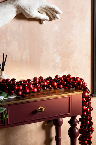 The Red Bauble Cluster Christmas Garland displayed draped on a console table, styled with some accessories.