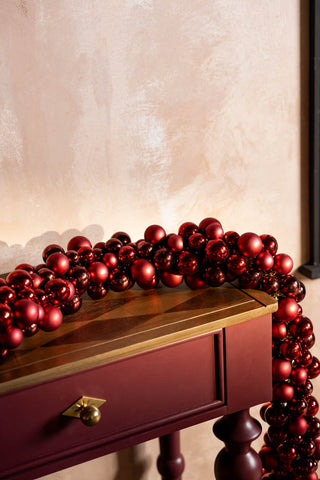 The Red Bauble Cluster Christmas Garland styled on a red and wooden console table.