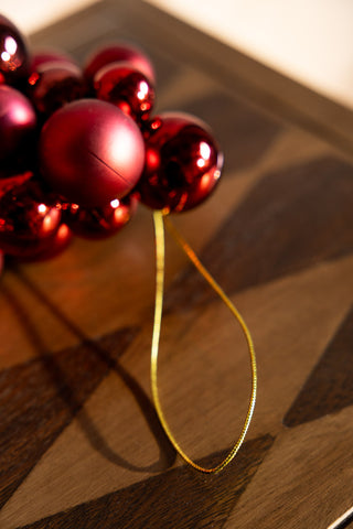 Close-up of the hanging loop on the end of the Red Bauble Cluster Christmas Garland, displayed on a wooden surface.