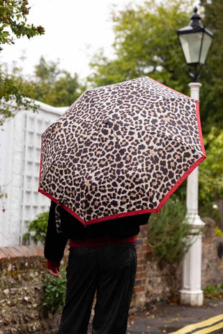 The Leopard Compact Umbrella shown from the back with a model walking down the street in the rain. 