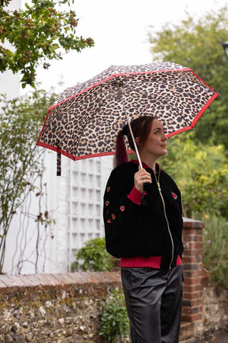 The Leopard Compact Umbrella shown with a model wearing black and red. 