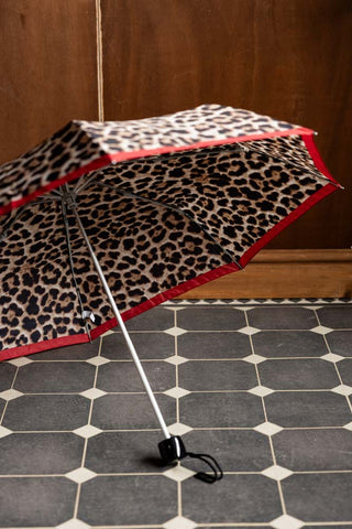 The Leopard Compact Umbrella shown open inside against a wood wall. 