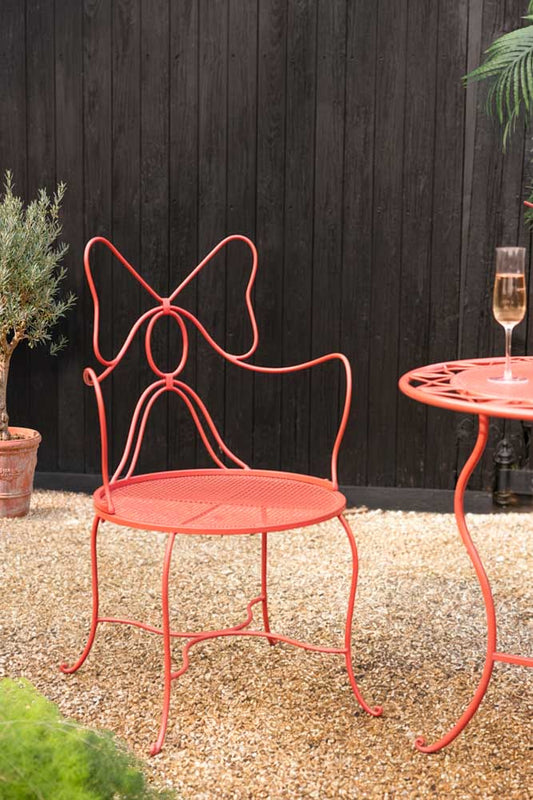The Red Bow Folding Garden Table & Chairs Set on an outdoor area with some plants.