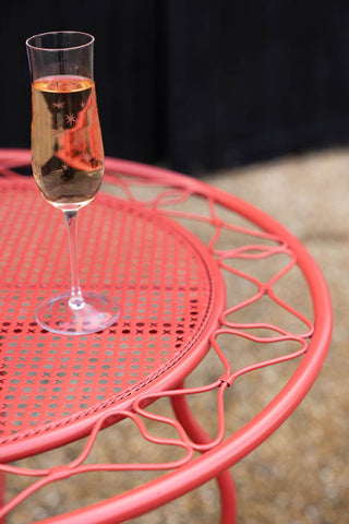 Close-up of the Red Bow Folding Garden Table & Chairs Set with a champagne glass on.