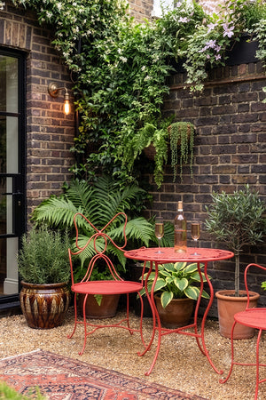 The Red Bow Garden Table & Chairs Set shown in a courtyard garden next to crittal doors. 