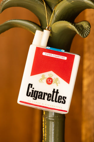The Red Cigarette Pack Christmas Tree Decoration styled on a ceramic palm tree candlestick holder.