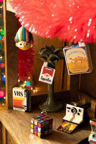 The Red Cigarette Pack Christmas Tree Decoration styled with various other decorations on a wooden sideboard.