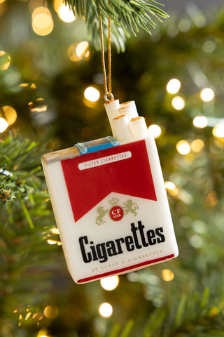 The Red Cigarette Pack Christmas Tree Decoration hanging from a Christmas tree with fairy lights in the background.
