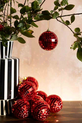 The Red Disco Ball Christmas Tree Decoration styled hanging from a branch  inside a vase.