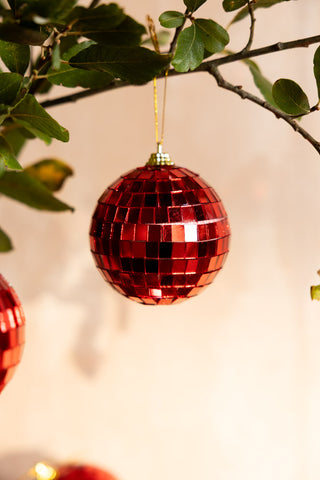 The Red Disco Ball Christmas Tree Decoration styled hanging from a branch.