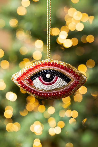The Red Eye Beaded Hanging Christmas Tree Decoration hanging in front of blurred fairy lights.