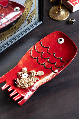 The Red Fish Serving Dish styled with a necklace inside, styled on a dark surface with some other accessories.