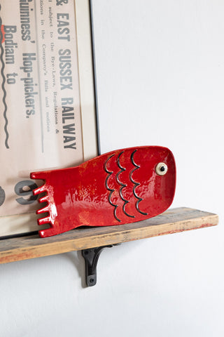 The Red Fish Serving Dish displayed on a shelf with a framed artwork.