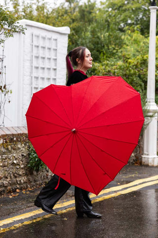 The Red Heart Umbrella shown outside in the street in the rain. 